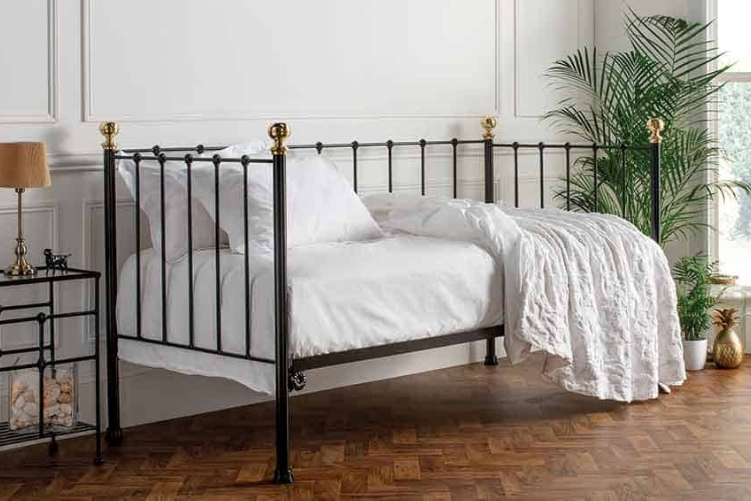 Garce black day bed with antique brass finials styled in a classic white bedroom with parquet flooring