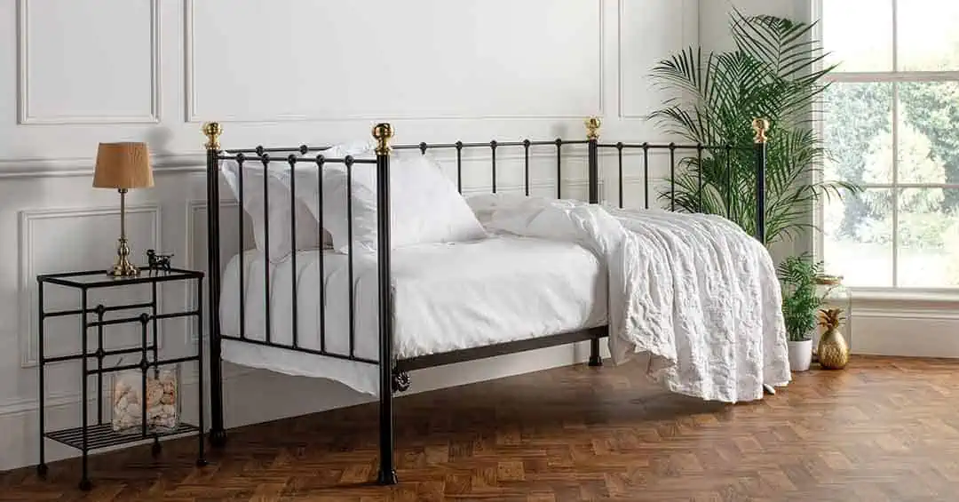 Garce black day bed with antique brass finials styled in a classic white bedroom with parquet flooring