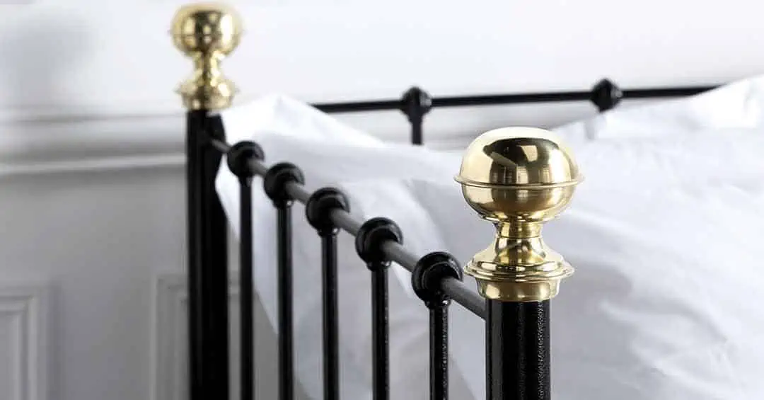 Close-up of Garce day bed featuring ornate antique brass finial and matte black metal posts with white bedding