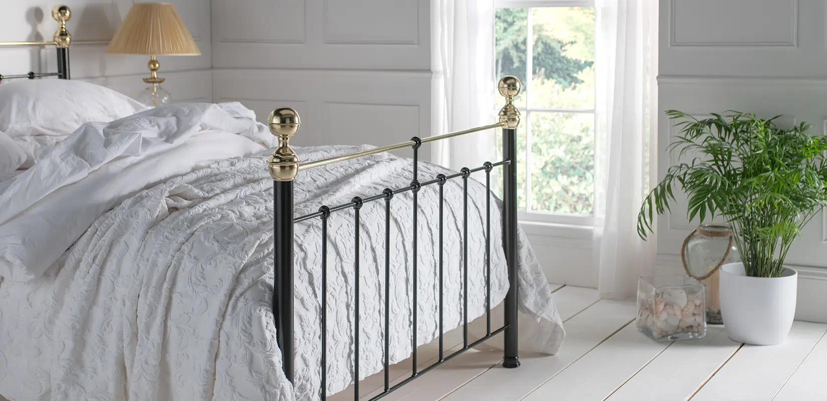Close-up of Albert bed headboard showing black vertical spindles and polished brass top rail with finial