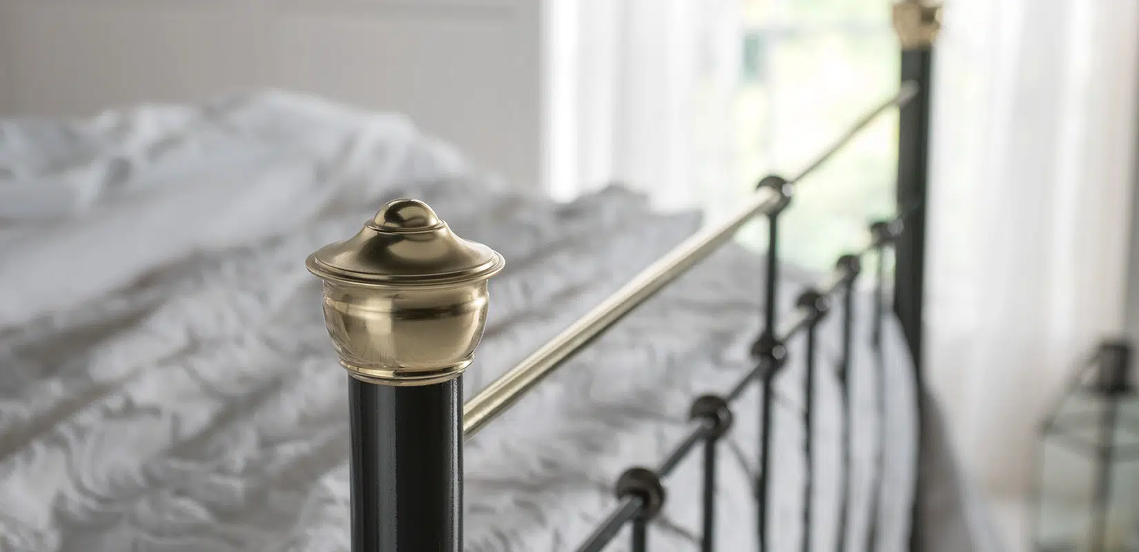 Close-up of Beatrice bed brass finial and horizontal rail against soft white bedding