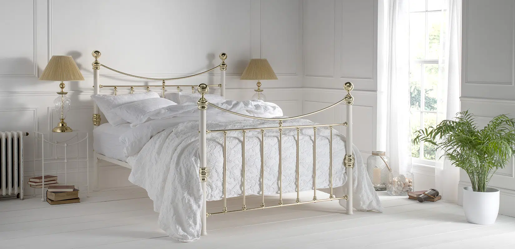 Elizabeth brass bed frame with curved top rail and ornate finials in a white airy bedroom