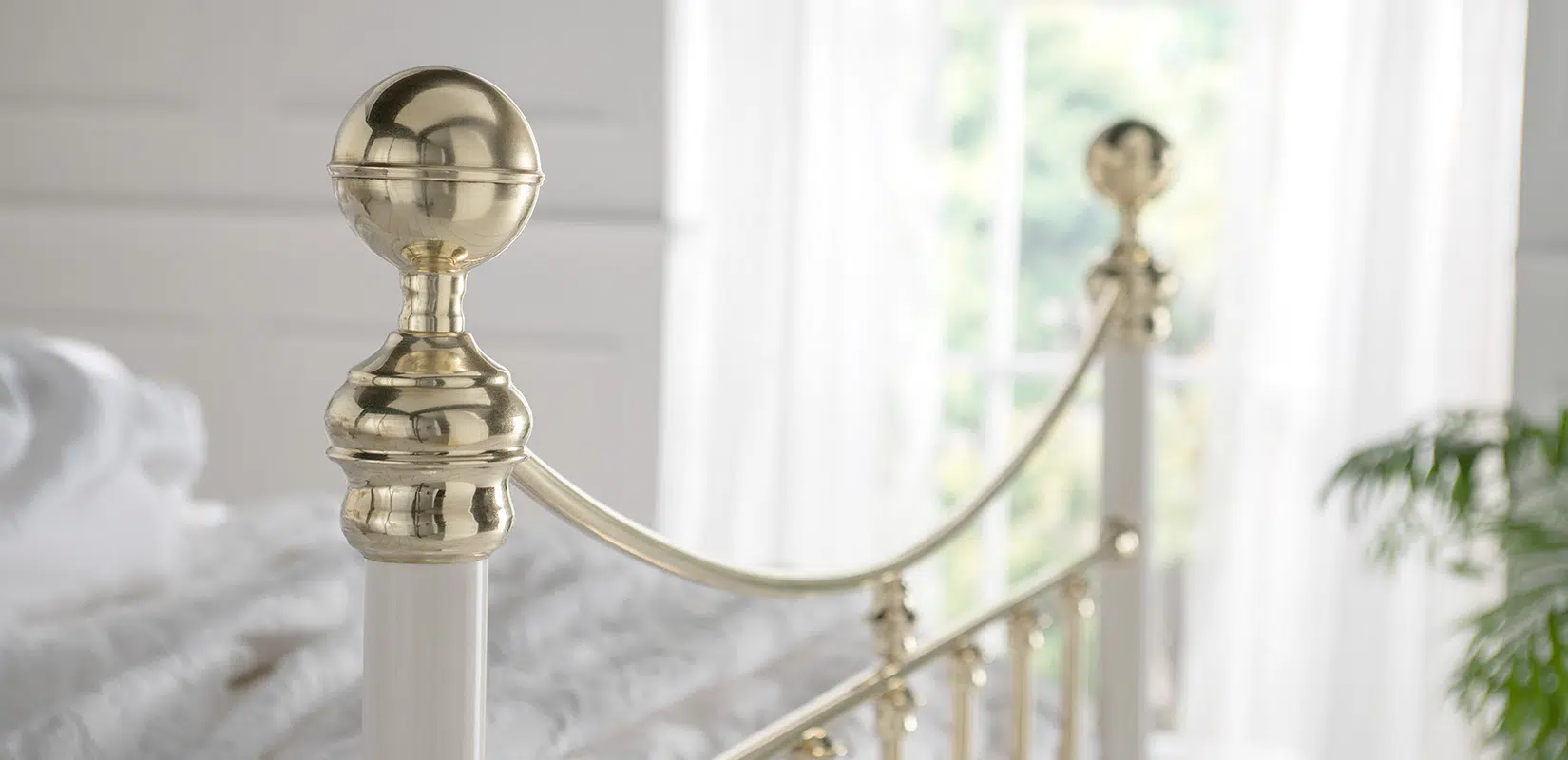 Zoomed-in detail of the Elizabeth brass bed finial and gentle curved rail with reflective surface