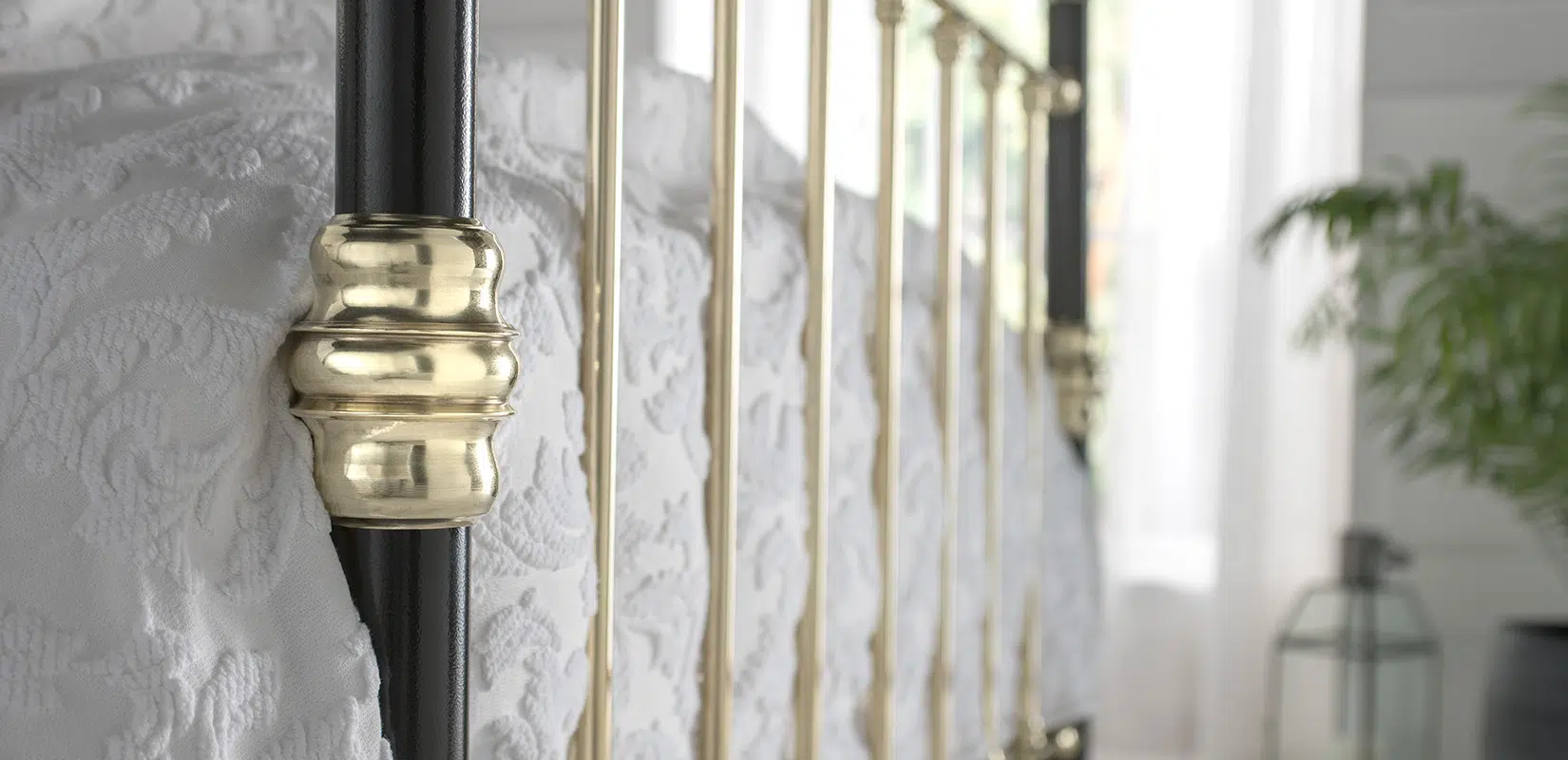 Close-up of George bed’s polished brass side rails against white quilted bedding