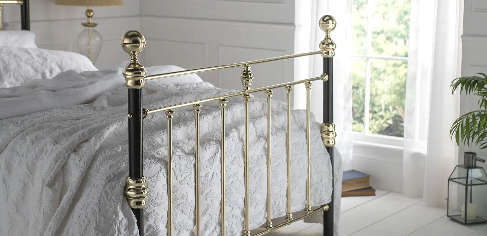 Side view of George bed showing vertical brass rails and black iron frame with white bedding