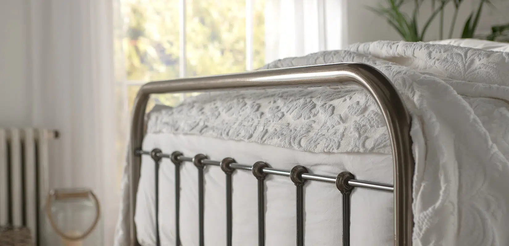 Close-up of Edward bed’s smooth round finial and softly curved top rail in a warm-toned setting