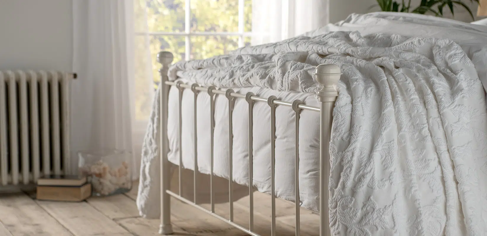 Side view of Grace bed’s footboard with gentle antique detailing and turned finials