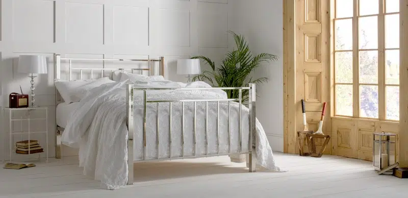 polished nickel iron bedframe - image is of a iron bedframe finished in polished nickel with chrome detailing, dressed in a woft white bedlinen