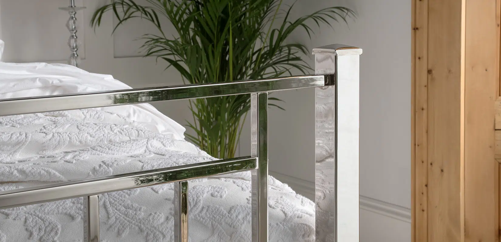 Nickel bed footboard with minimalist design and square edges, placed in a plant-filled bedroom