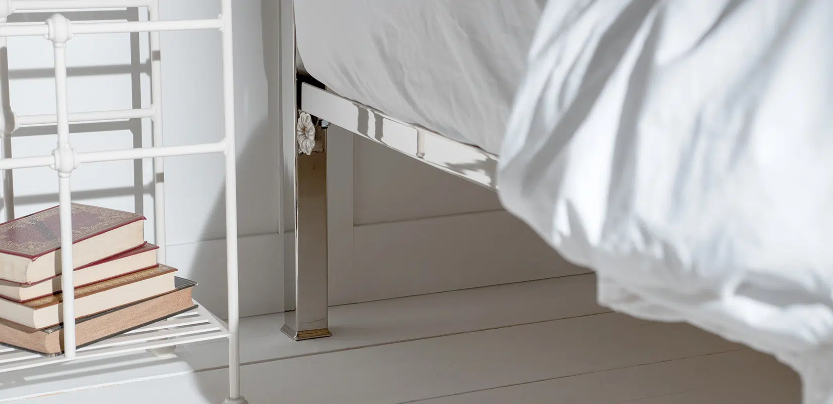 Close-up of polished nickel bed frame with headboard and visible underbed space in white wood flooring