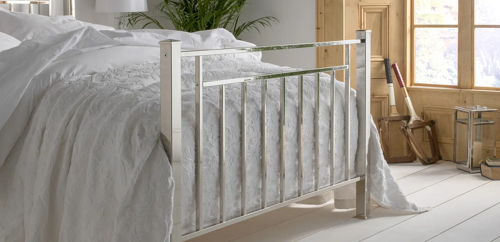 Corner detail of a polished nickel bed frame, showcasing vertical bar design and reflective surface