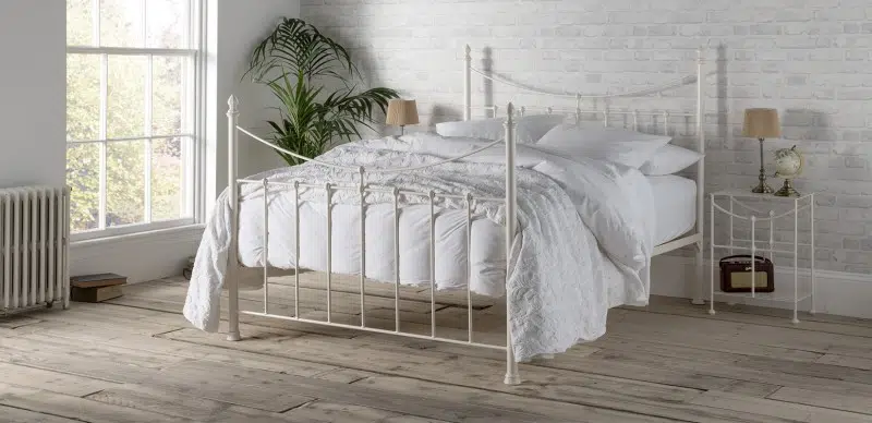 elegant iron bed in a soft white finish - the image is of an iron bed that features a down sweeping curve finished in a soft white powder coated finish, dressed with white bedlinen