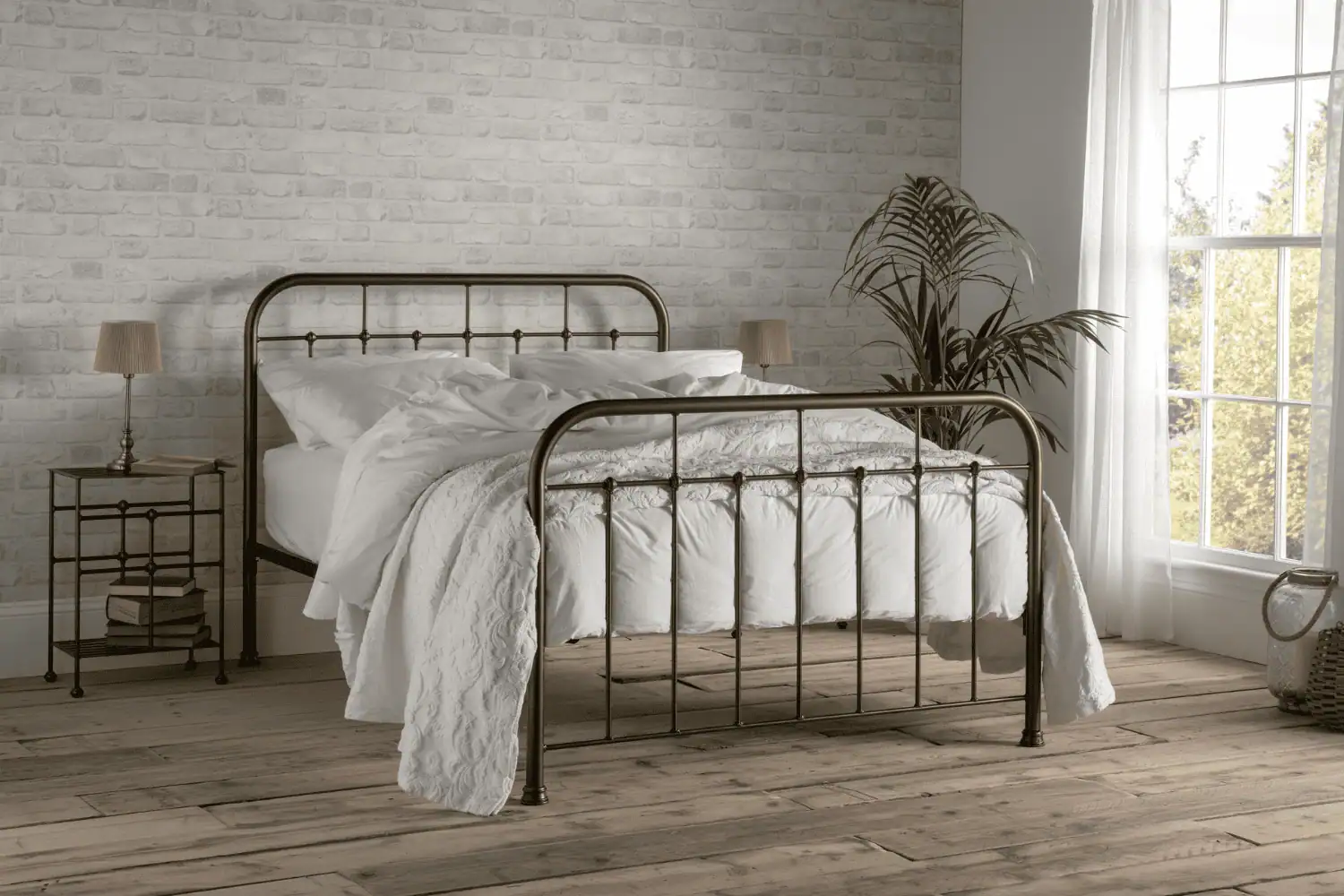 Henry iron bed frame in a warm bronze finish, styled in a cosy brick-wall bedroom with white bedding and wooden floors