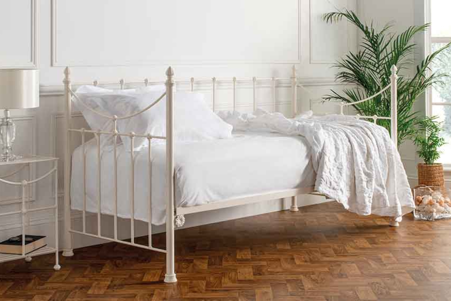 Emily ivory day bed with ornate metal frame styled with white bedding in a bright, minimalist bedroom with parquet flooring