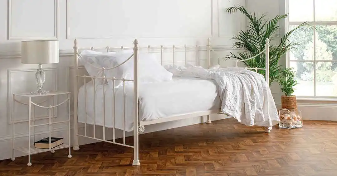 Emily ivory day bed with ornate metal frame styled with white bedding in a bright, minimalist bedroom with parquet flooring