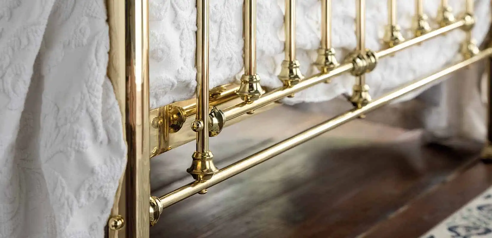 Base section of Willow brass bed showing traditional turned legs and rail design on wooden floor