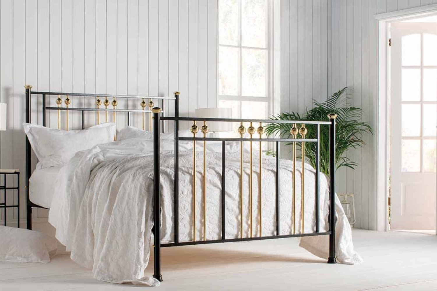 Dolly brass and black iron bed in a sunlit bedroom with white bedding and neutral decor