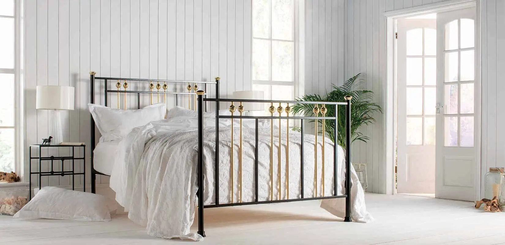 Dolly brass and black iron bed in a sunlit bedroom with white bedding and neutral decor