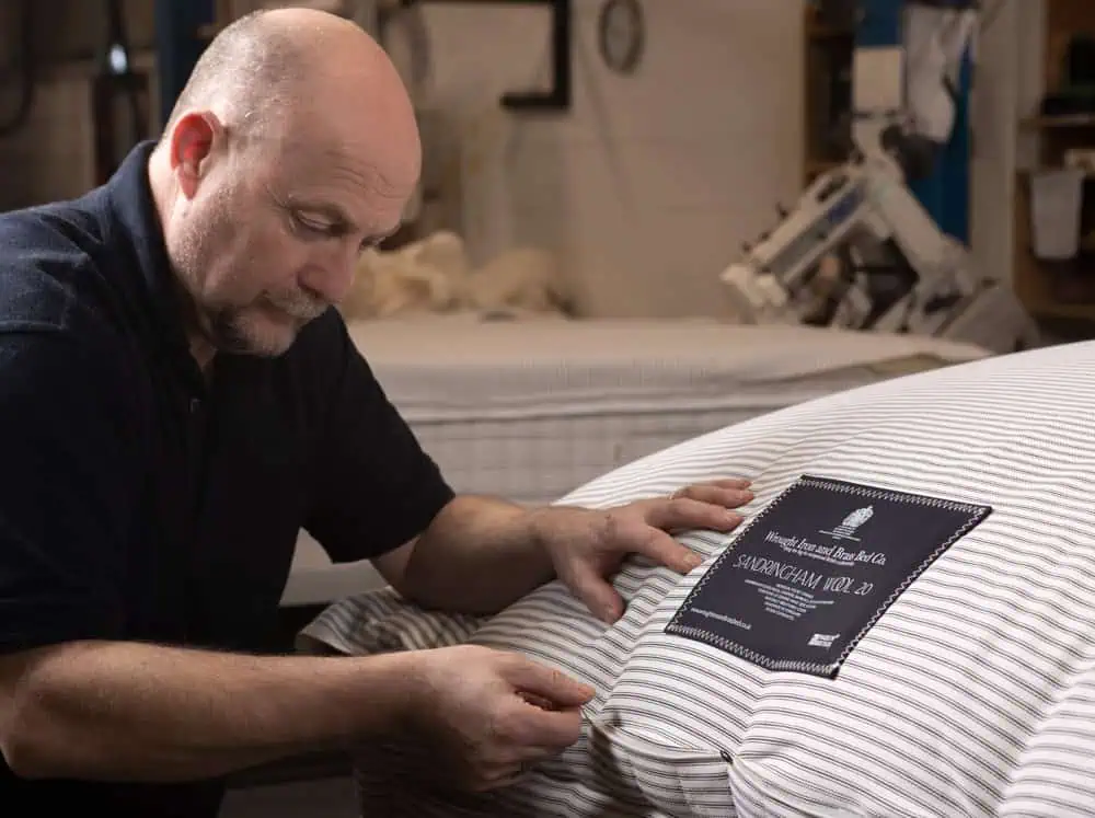 Craftsman hand-finishing a luxury mattress with striped ticking and Royal Warrant label in a workshop setting