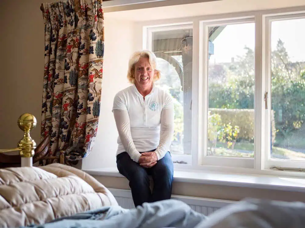 image of amanda oldfield founder of wrought iron and brass bed company sitting on a window sill of a bedroom which features the comonay signature brass bed, george. 