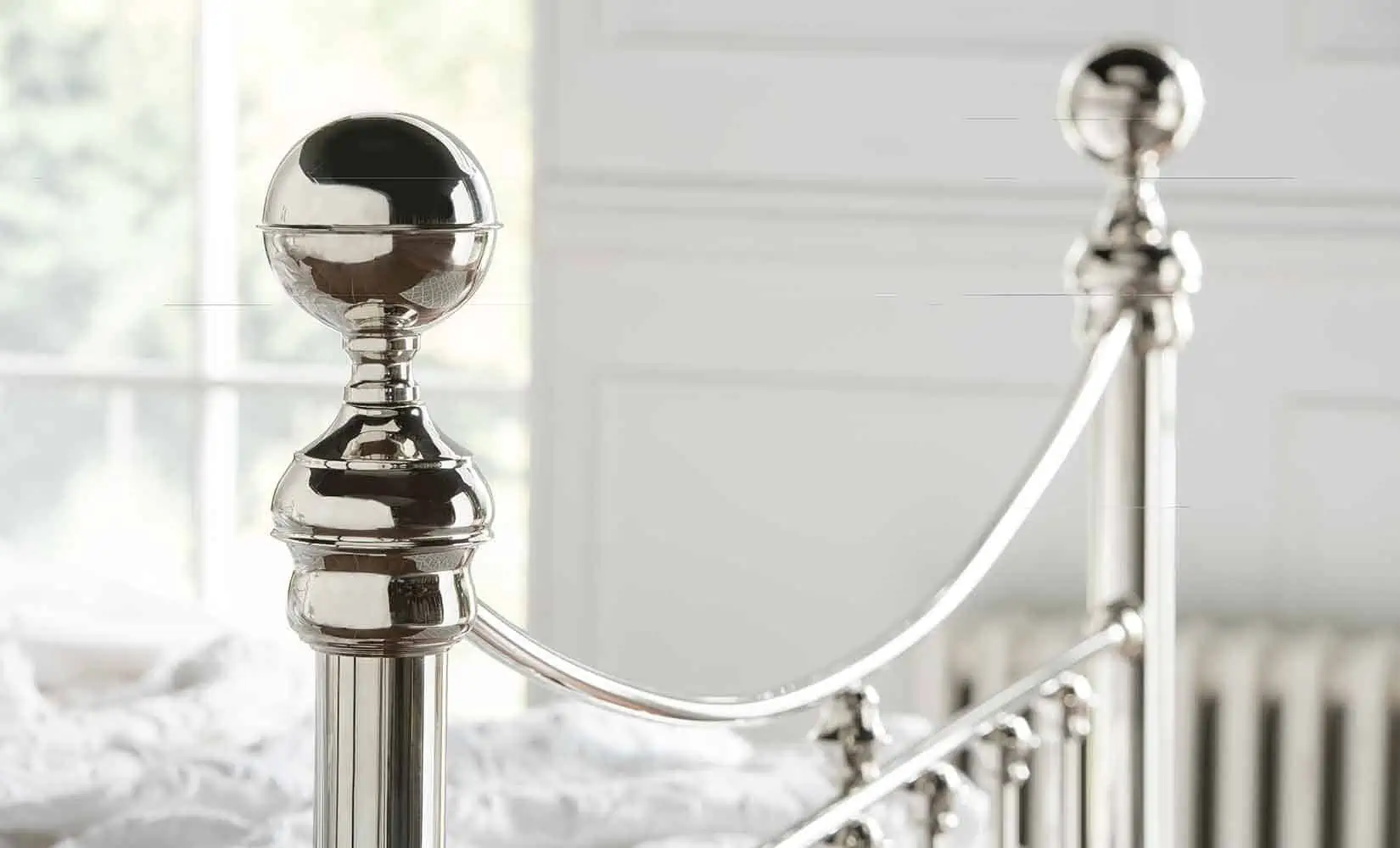 Detail of Alice bed’s nickel finial and sweeping curved rail, reflecting soft natural light