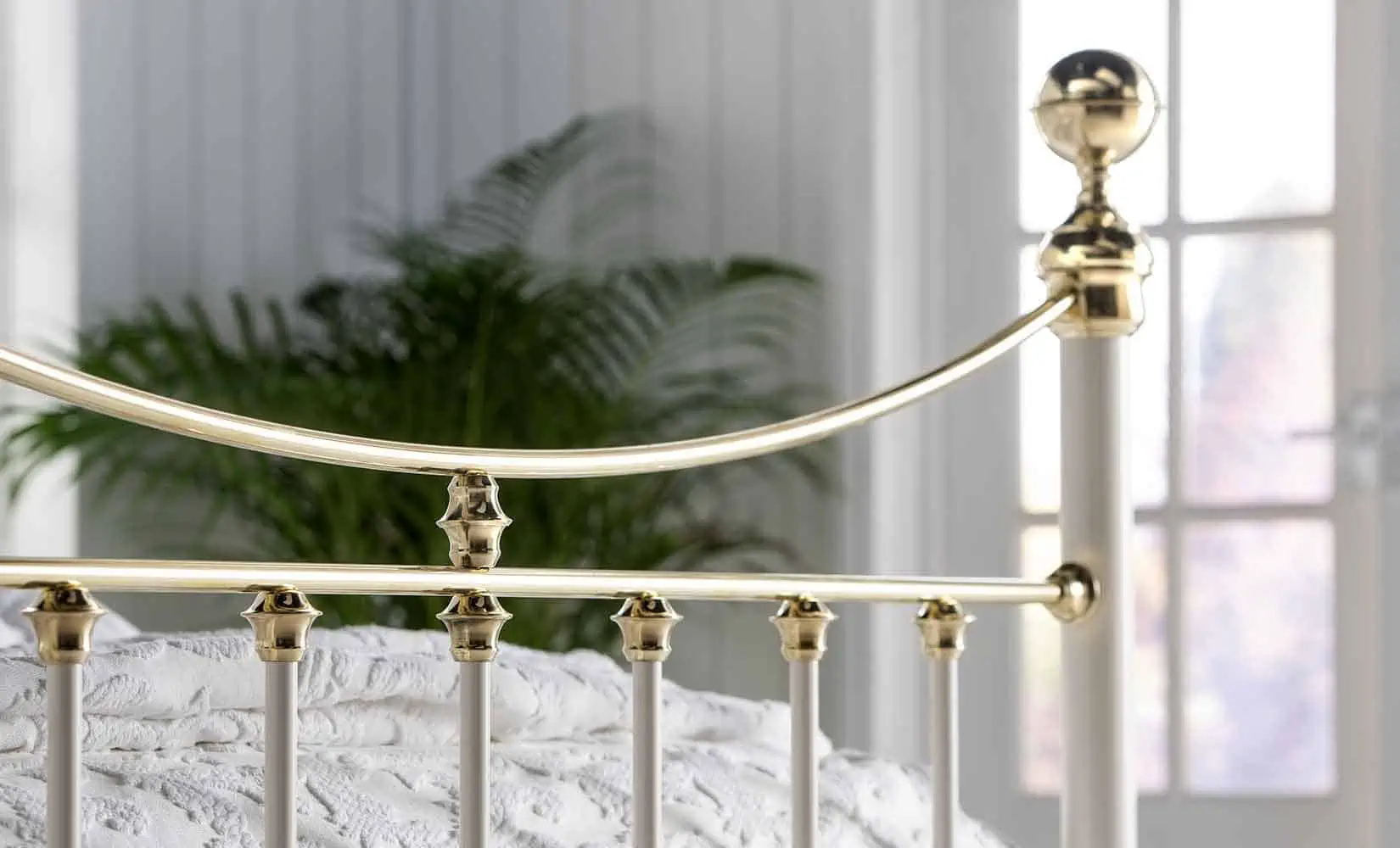 Detailed shot of Lottie brass bed's polished curved rail and finial craftsmanship