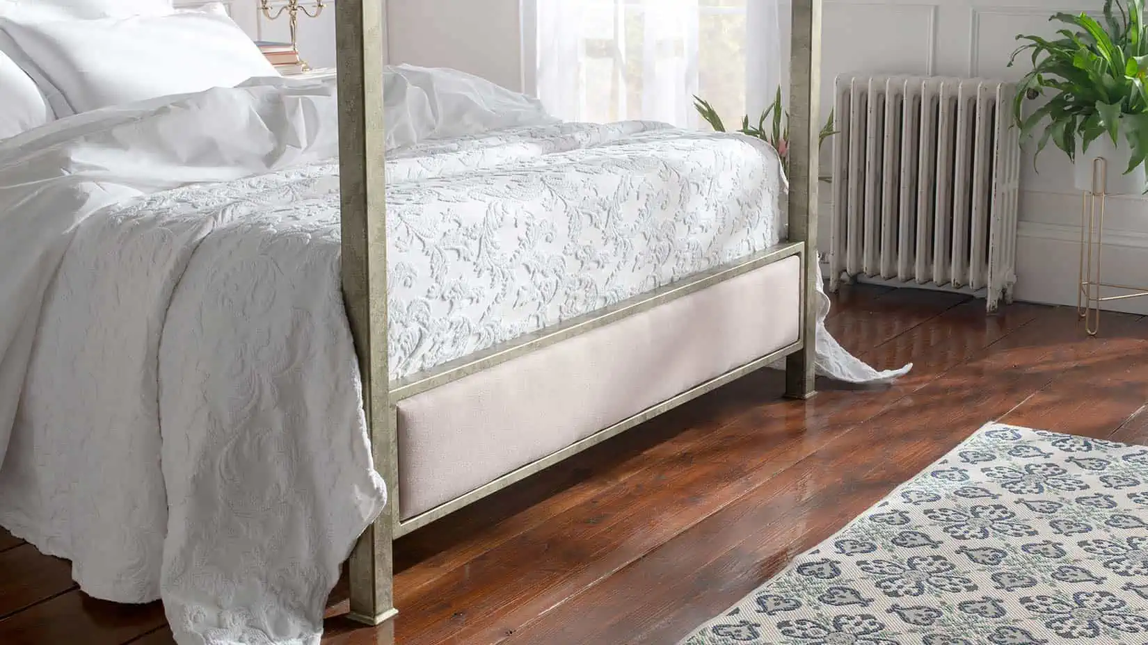 Aurora four-poster bed with blush upholstered footboard and antique gold frame, styled with floral bedding