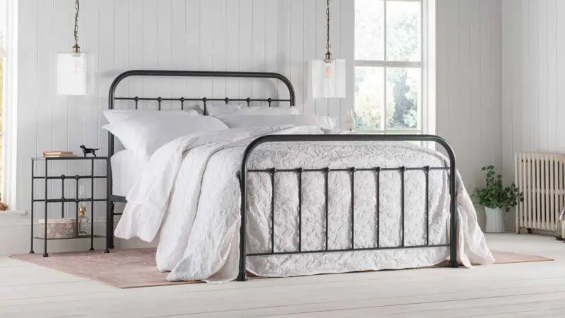 black iron bedframe - this image is of a black iron bedframre that features a down sweeping curve, the bed is dressed in white bed linen to show off the iron bedframe