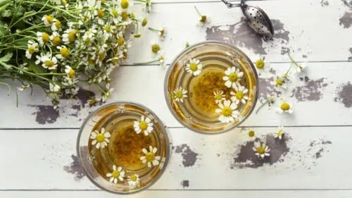 Top view of two cups of chamomile tea with fresh chamomile flowers on a rustic wooden table — a natural remedy for better sleep and relaxation.
