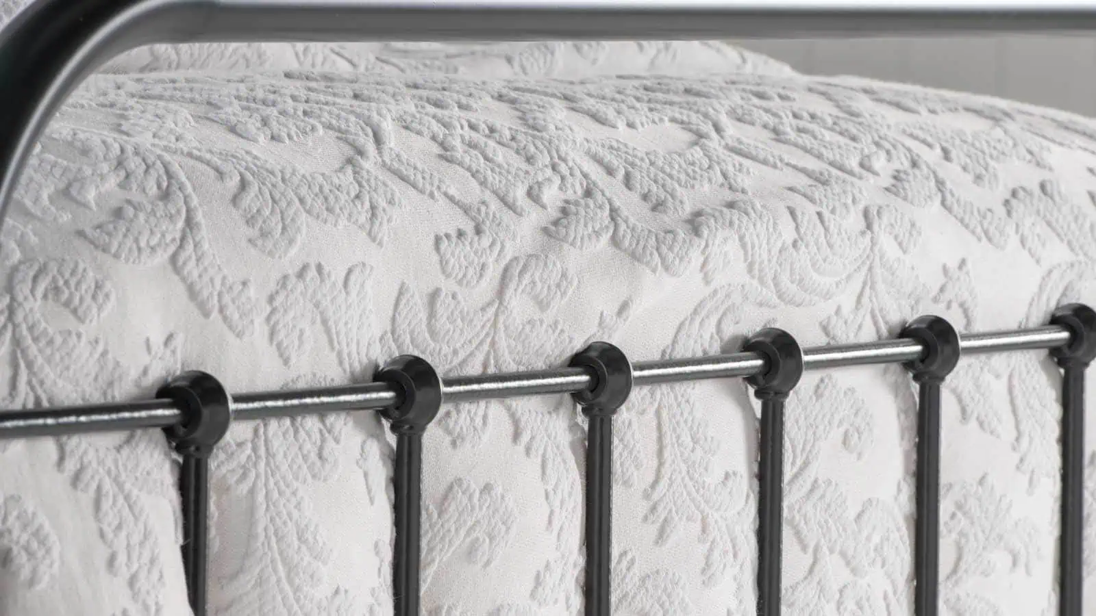 Close-up of Archie bed’s iron bar detailing against embossed white bedspread