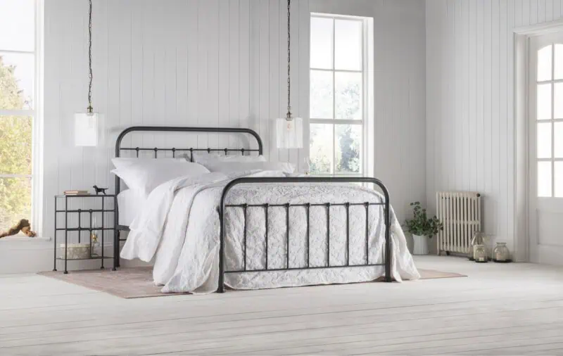 Black dorm-style iron bed frame in a light cottage style bedroom with white bedding, panelled walls, and soft neutral textures
