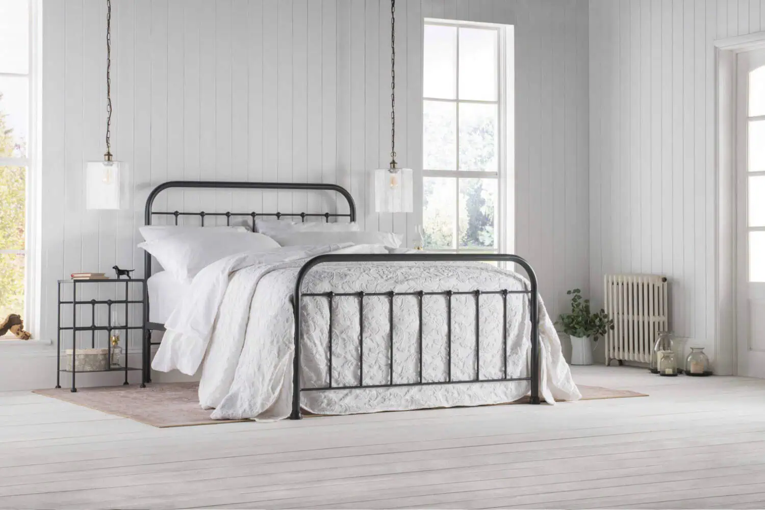 Full view of Archie iron bed with rounded headboard and vertical bars in a bright white bedroom