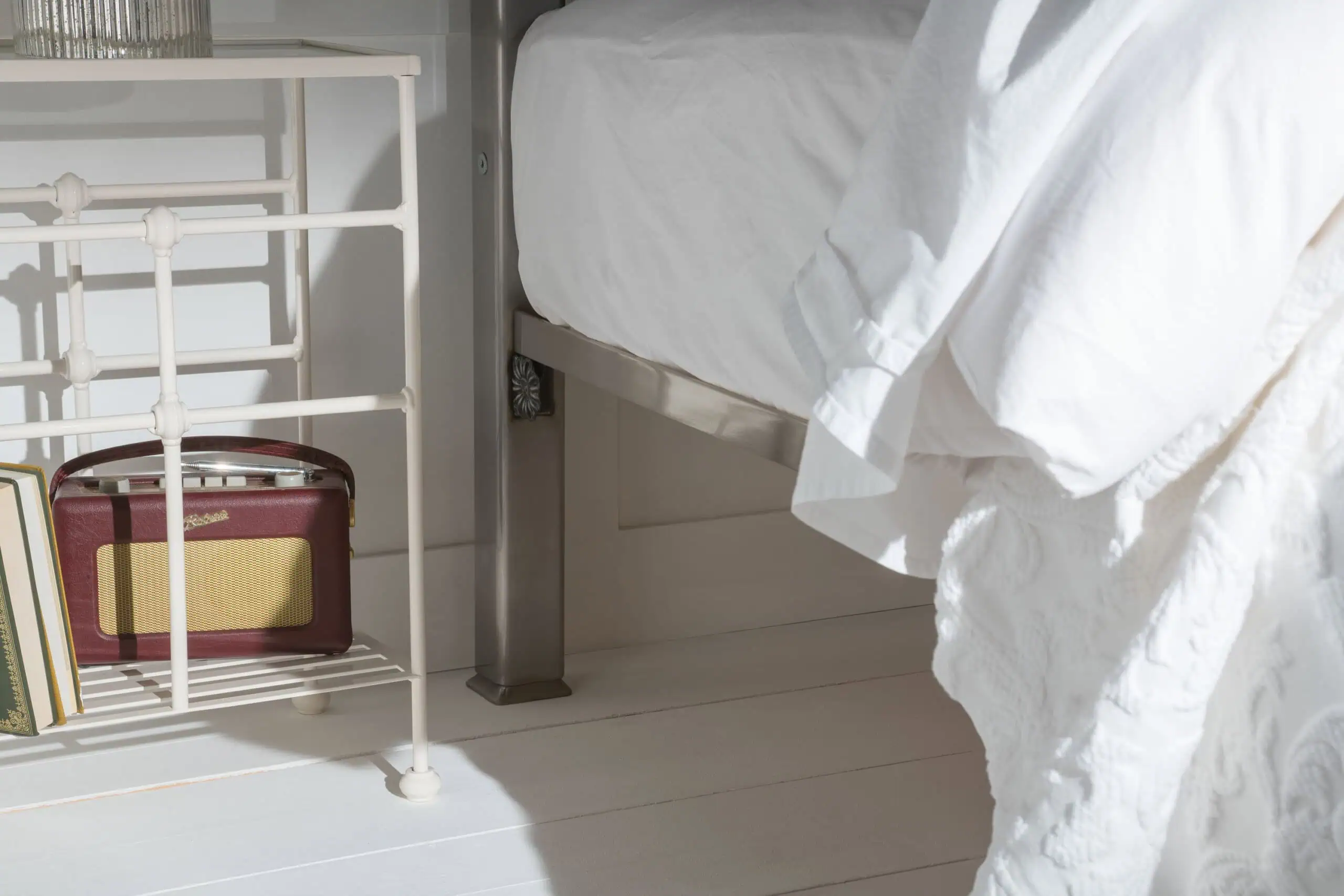 Close-up of Louis bed’s underframe with brushed metal legs and white bedding, showing storage space beneath