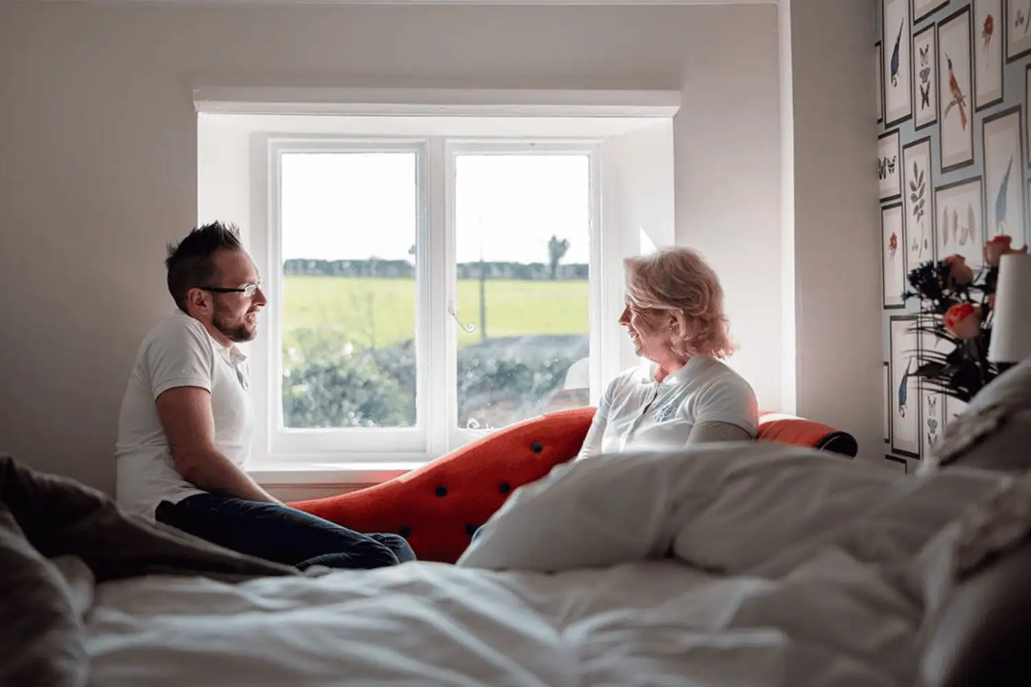 Harry and Amanda sitting on a handmade iron bed, talking by the window in a light-filled bedroom