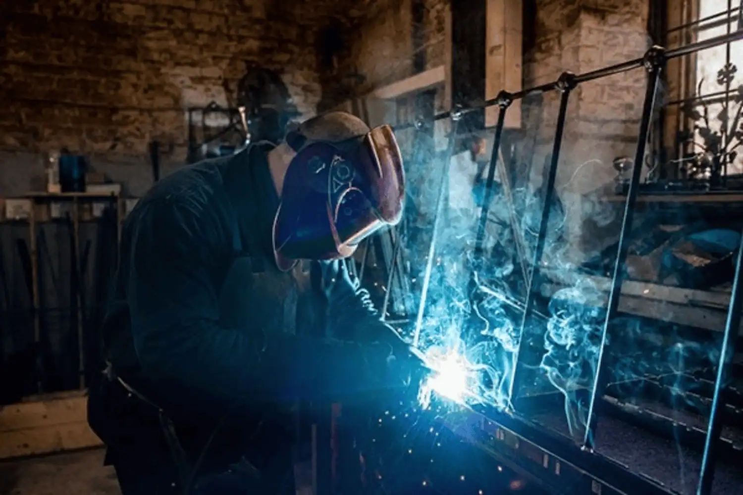 Skilled craftsman welding a handmade iron bed frame in the Norfolk workshop