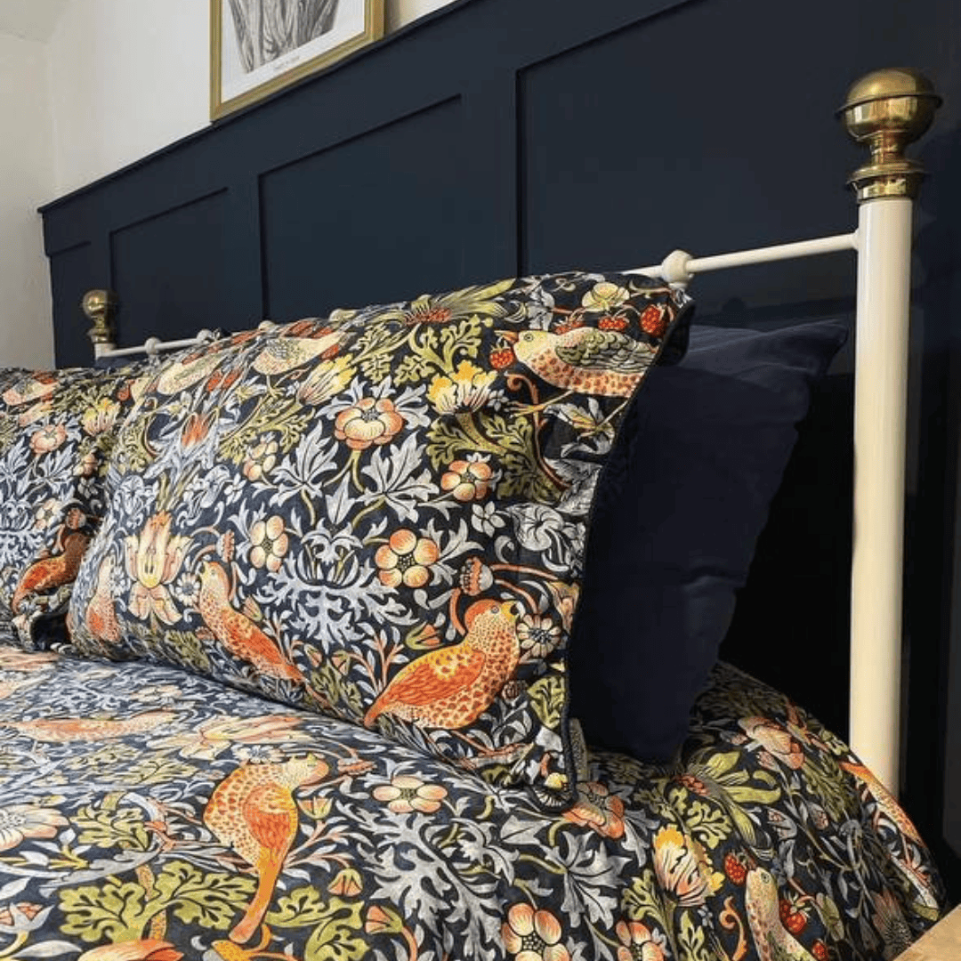 A metal bed frame with a richly patterned quilt in warm autumnal colors, styled in a modern bedroom.