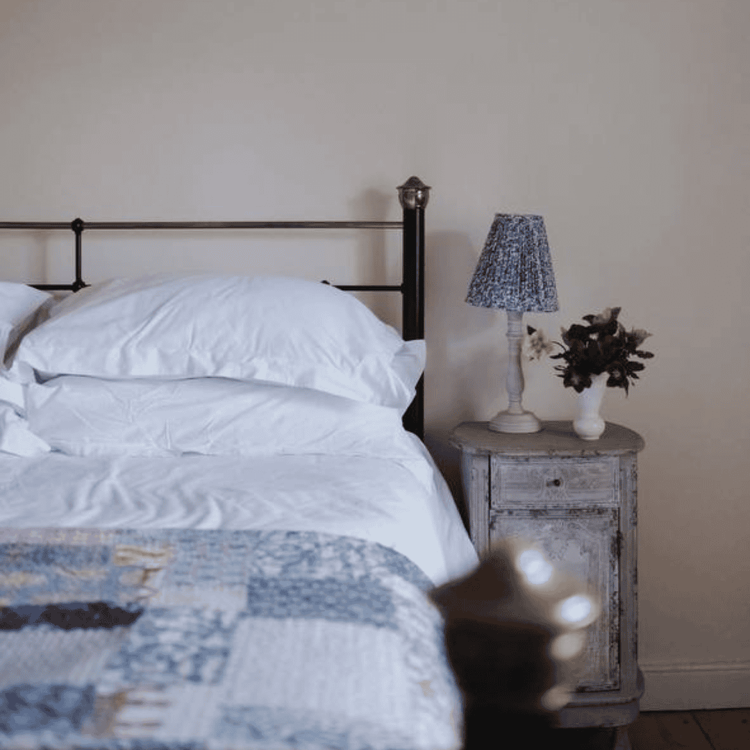 A minimal metal bed frame with crisp white bedding, accompanied by a silver bedside table and small potted plant.