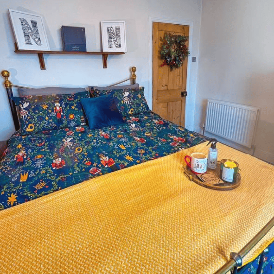 A vibrant bedspread with floral patterns and a mustard throw in a bright bedroom with white walls.