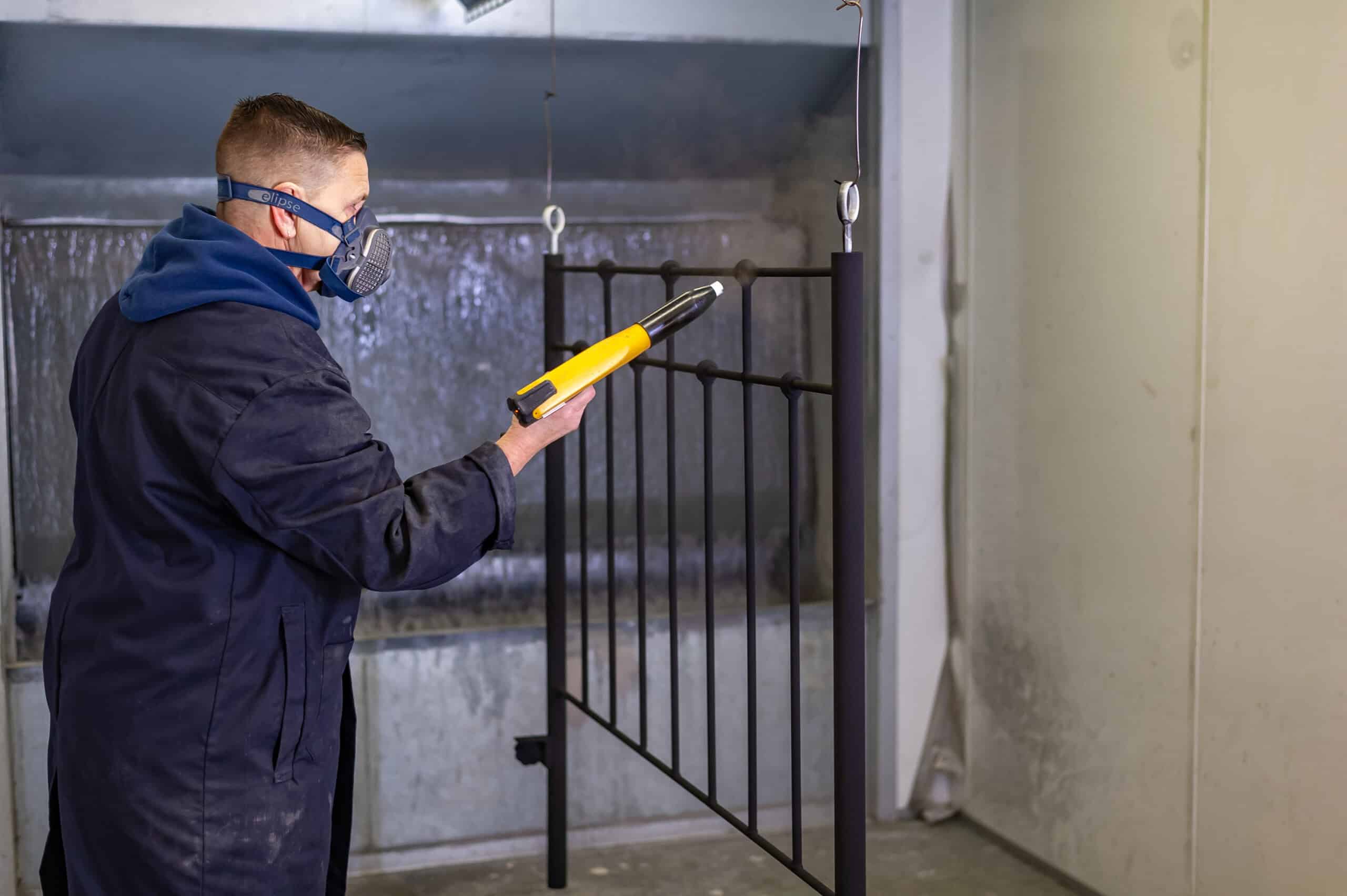 Quality Inspection of Iron Bed Frames Skilled worker wearing safety gear inspecting a black iron bed frame with a measuring tool.