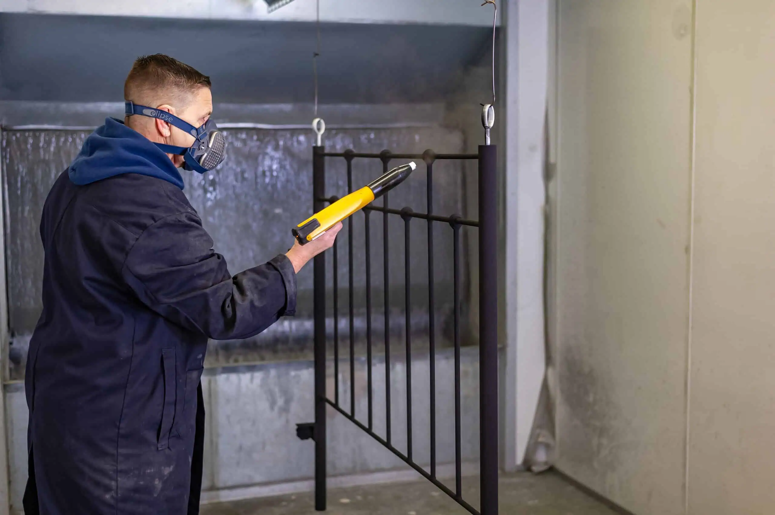 Skilled worker wearing safety gear inspecting a black iron bed frame with a measuring tool.