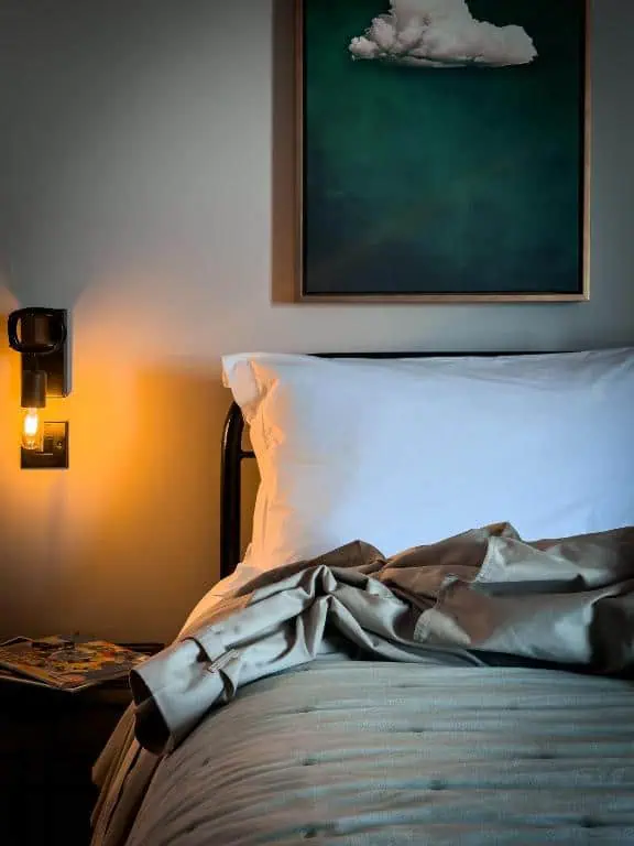 834458579 iron bed frame dressed in white bedding - this image is our iron and brass bed companys henry dorm style iron bed frame finished in a bronze powder coated finish