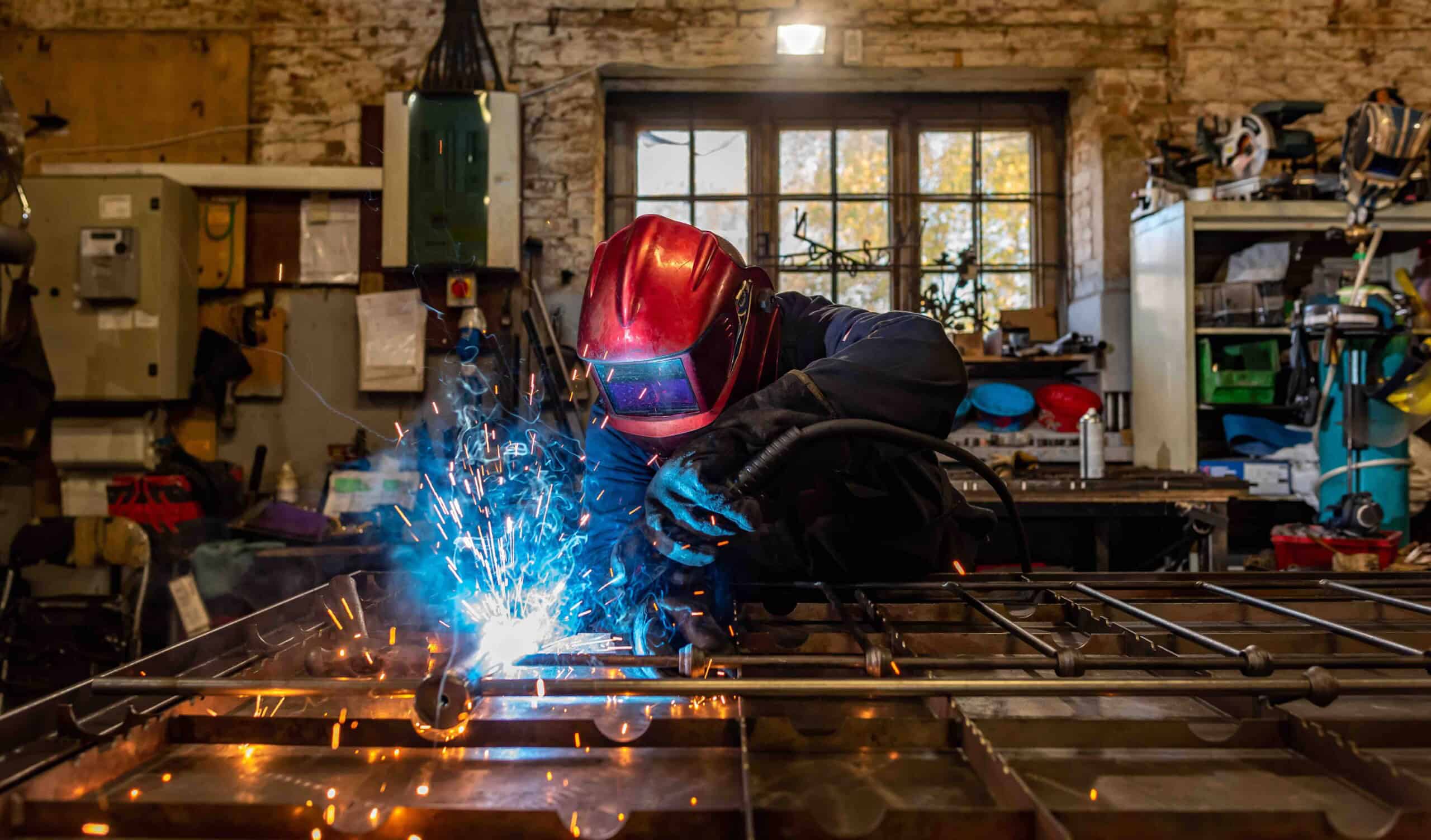Craftsman welding a handcrafted metal bed frame in our Norfolk workshop