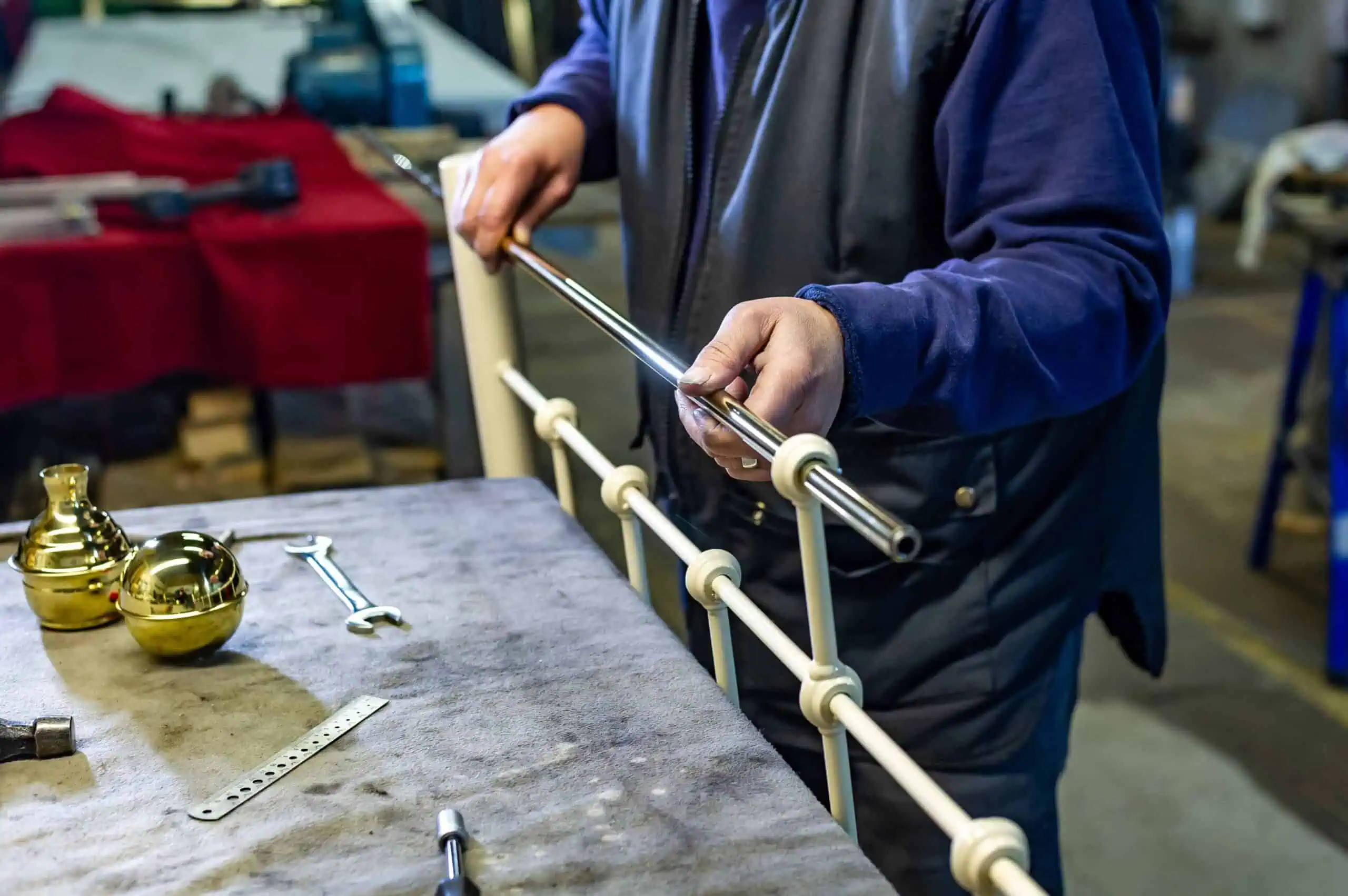 Craftsman assembling a wrought iron and brass bed frame in workshop.