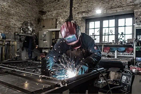 Craftsman welding wrought iron for custom bed frames in workshop.