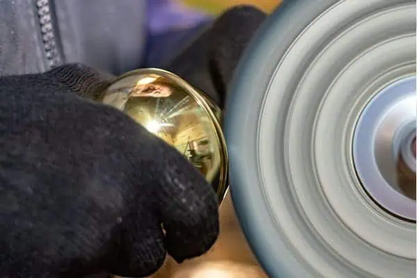 Close-up of a brass bed finial being polished with a power tool.